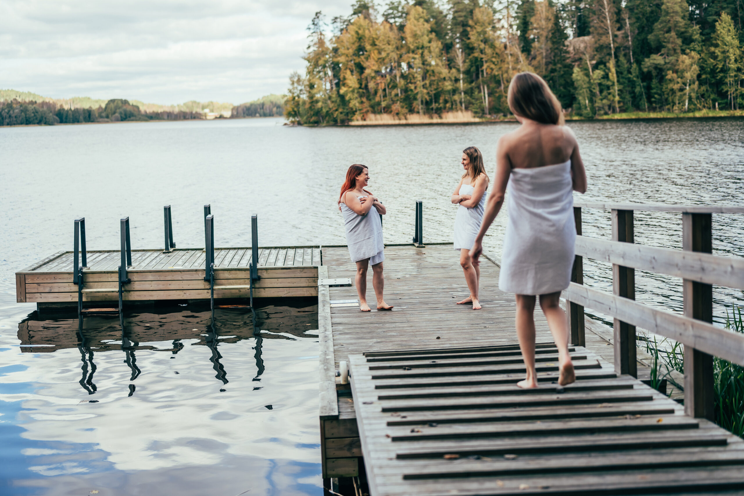 Kolme naista seisoo laiturilla pyyhkeet yllään.